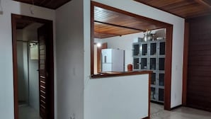Eine Küche mit weißer Arbeitsplatte, einem Kühlschrank und einem Herd. Die Decke ist aus Holz und es gibt eine Tür zu einem anderen Raum.