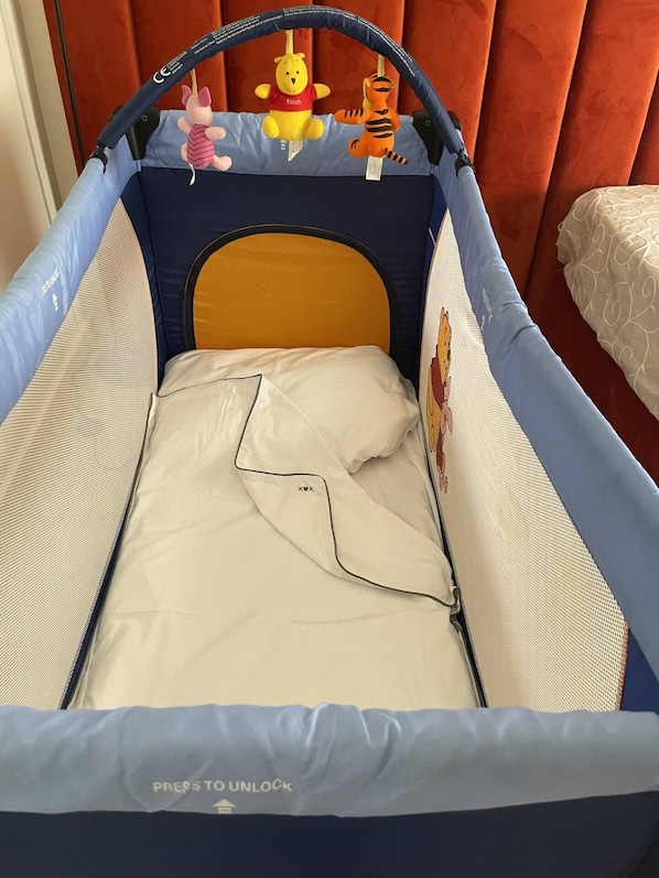 Een babybedje met een zachte matras, een hoofdbord en een veiligheidshek.