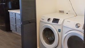 A laundry area with two white washing machines, a small shelf with bottles, and a grey cabinet with drawers.