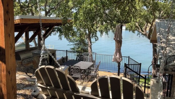 A deck with Adirondack chairs, a grill, and a table overlooking a lake.