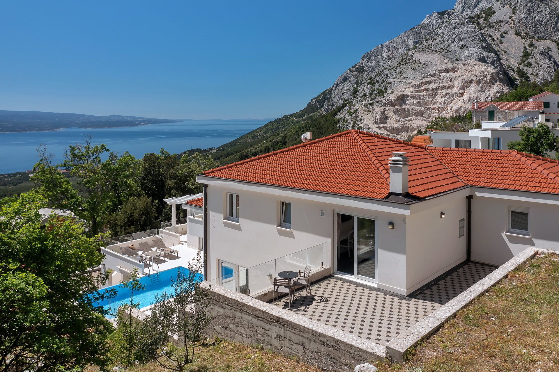 A modern two-story house with a red-tiled roof, a swimming pool, and a view of the sea and mountains.