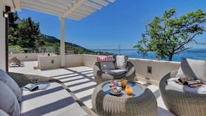 A terrace with wicker furniture, a table with drinks, and a view of the sea. - Villa Simply White with Pool (Makarska)