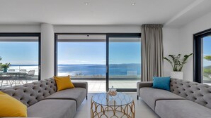 Una sala de estar moderna con dos sofás grises, una mesa de centro de cristal y vista al mar.