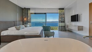 Un dormitorio moderno con una cama grande, una zona de estar, una bañera y un televisor.