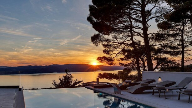 Zona junto a la piscina con sillas de descanso y vistas al atardecer sobre el agua.