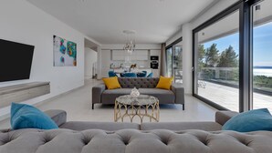 Una sala de estar moderna con un sofá gris, una mesa de centro de vidrio y un ventanal con vistas al mar.