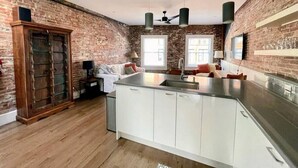 A modern kitchen with a large island, white cabinetry, and a brick wall.
