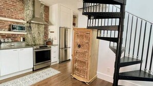 A modern kitchen with white cabinets, a brick accent wall, and a black spiral staircase.