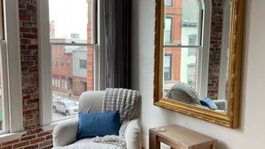 A room with a white armchair, a small wooden side table, and a large mirror on the wall. - Stunning Luxury Apt/Old Port Arts Dist/Sleeps8 (Portland)