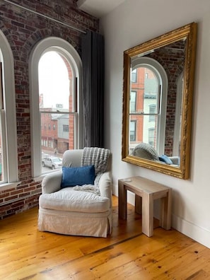 A room with a white armchair, a small wooden side table, and a large mirror on the wall. - Stunning Luxury Apt/Old Port Arts Dist/Sleeps8 (Portland)
