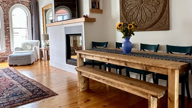 A spacious living room with a wooden dining table, a fireplace, and a large decorative wall piece. - Stunning Luxury Apt/Old Port Arts Dist/Sleeps8 (Portland)