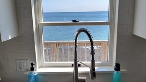 Cocina con ventana que da al mar, un lavamanos de acero inoxidable, dispensador de jabón y portalcepillos de dientes.