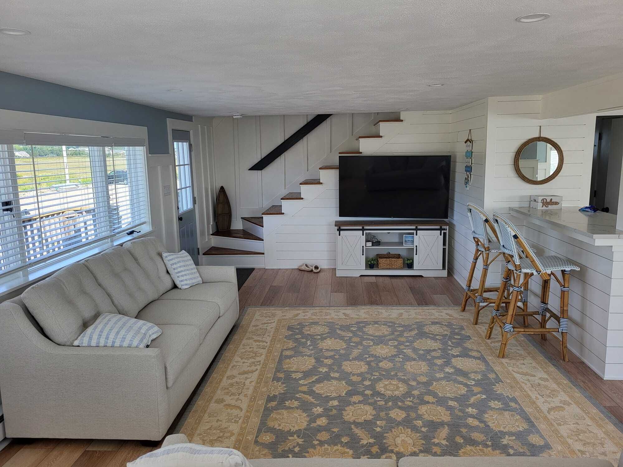 A living room with a sofa, a TV, a staircase, and a bar area.
