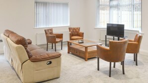 Una sala de estar moderna con un sofá color crema, sillones de cuero, una mesa de centro de madera y un televisor sobre un mueble.