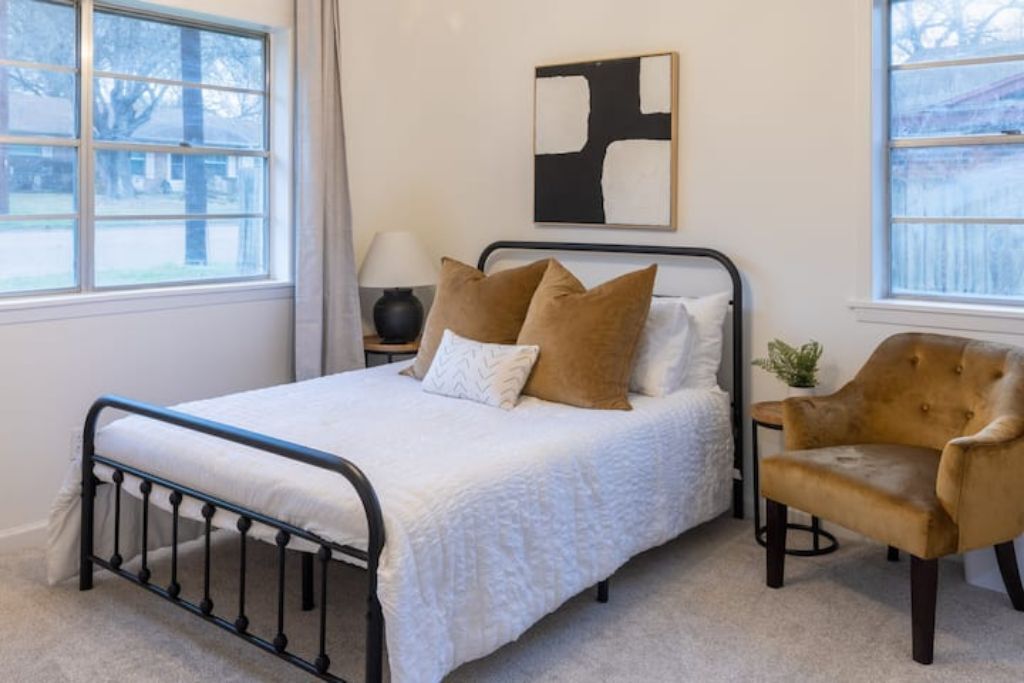 Une chambre à coucher avec un lit, une table de chevet, une lampe, une chaise et un tableau accroché au mur.