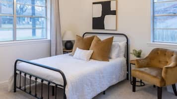 Une chambre à coucher avec un lit, une table de chevet, une lampe, une chaise et un tableau accroché au mur.