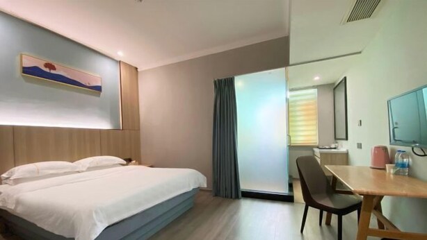 Une chambre d’hôtel avec un lit, un bureau, une chaise, une poubelle, une fenêtre avec des rideaux et un tableau au mur.
