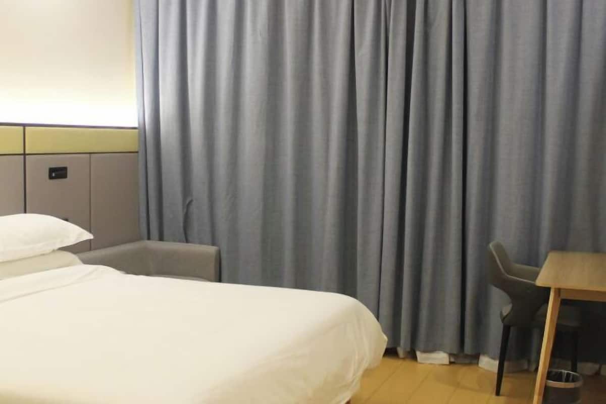 A hotel room with a bed, a desk, a chair, and a curtain.