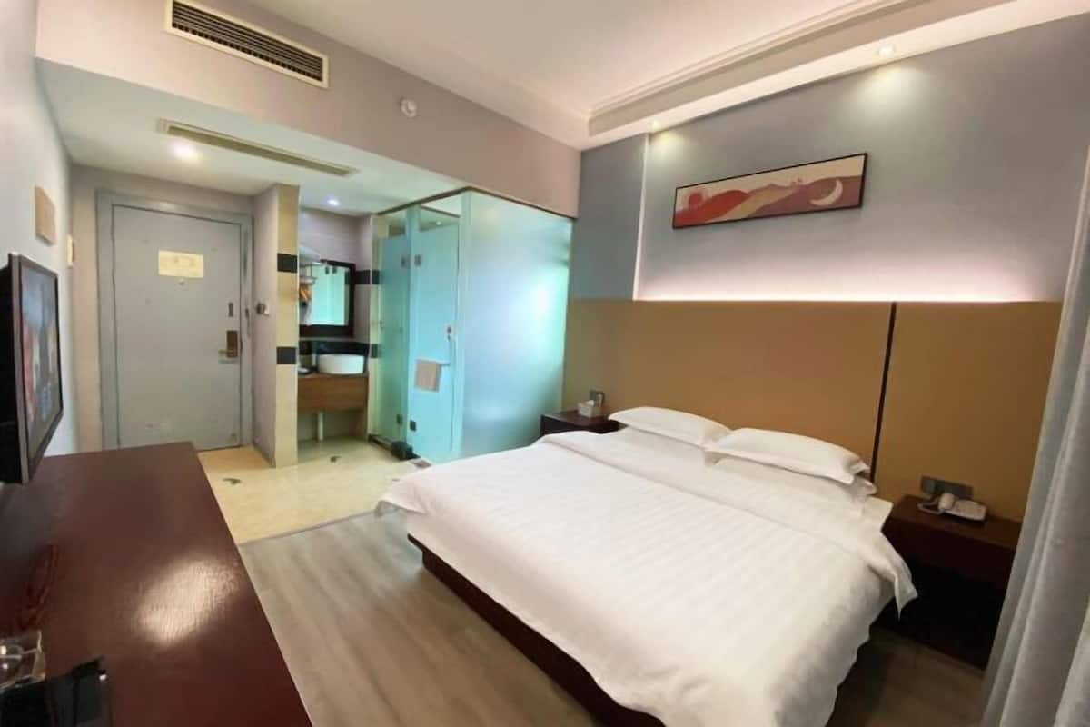 A hotel room with a bed, a desk, a chair, a television, and a bathroom visible through an open door.