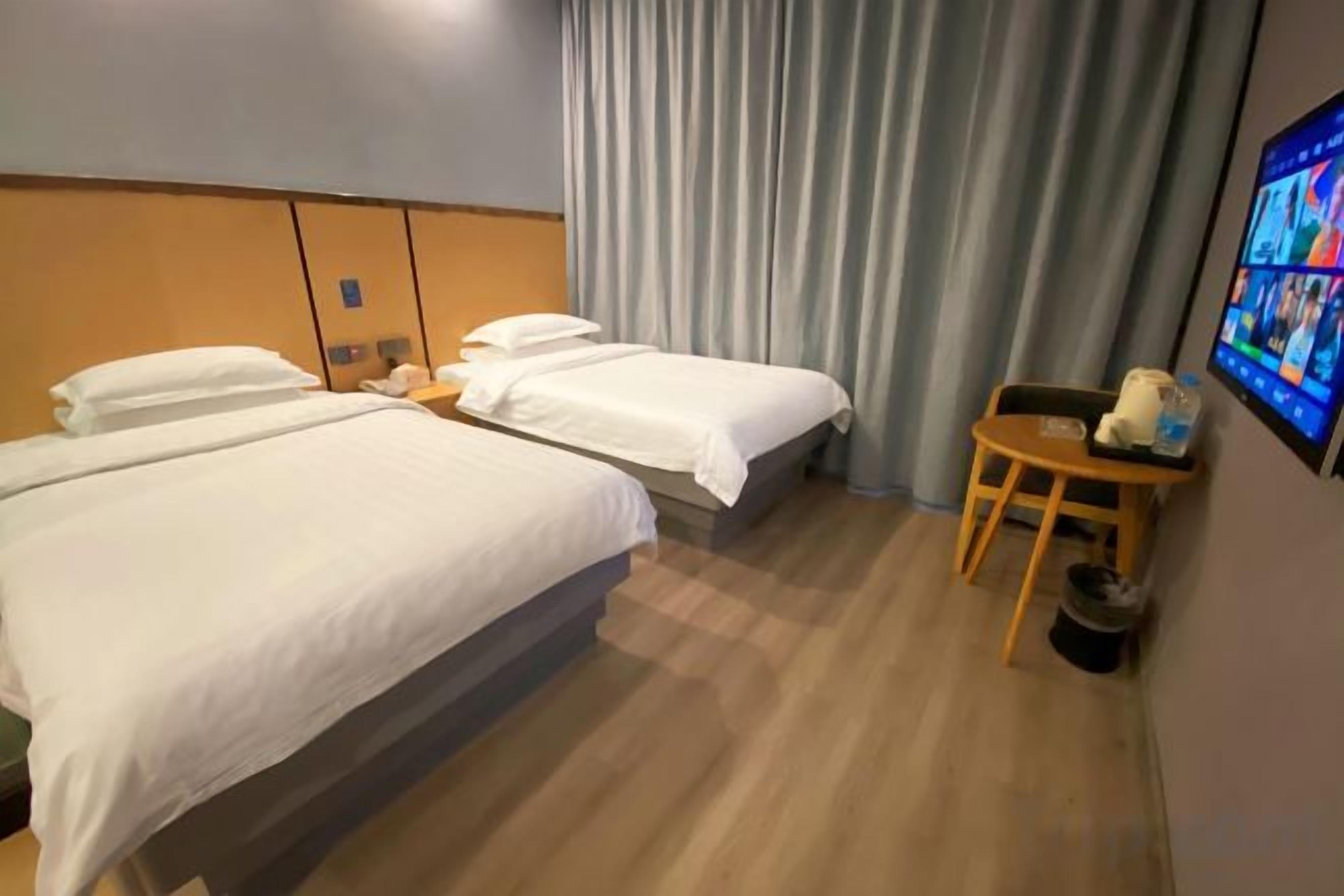 A hotel room with two beds, a small table, a chair, and a wall-mounted TV.