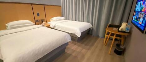 A hotel room with two beds, a small table, a chair, and a wall-mounted TV.