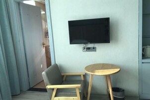 Una habitación con una televisión de pantalla plana en la pared, un sofá gris y una pequeña mesa de madera.