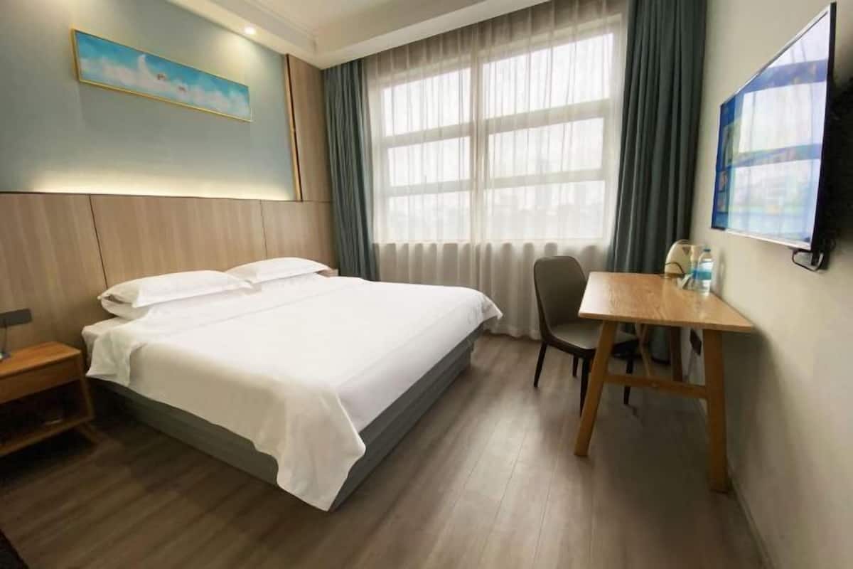 A hotel room with a bed, a desk, a chair, a TV, and a window with curtains.