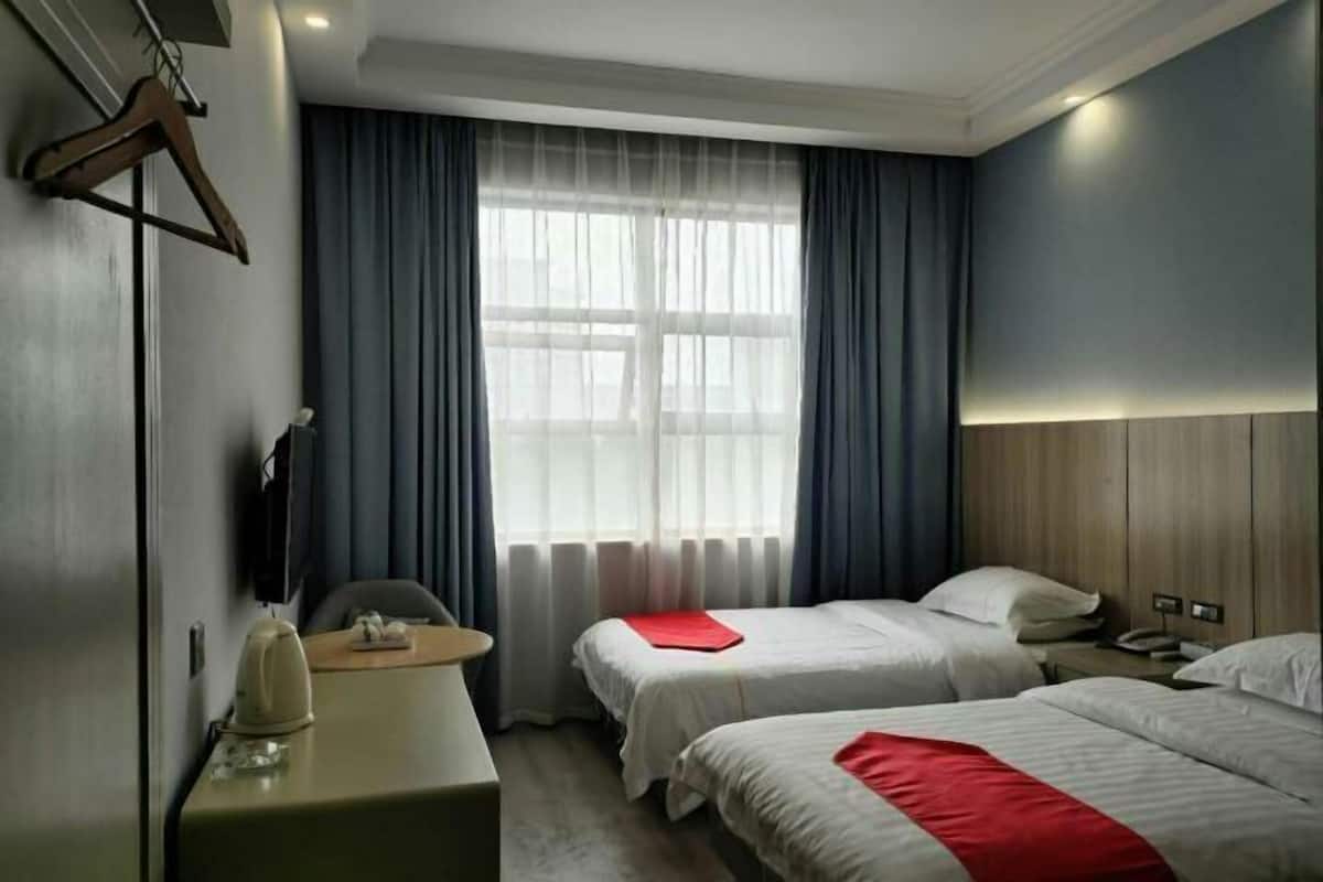 A hotel room with two beds, a desk, a chair, and a window with curtains.