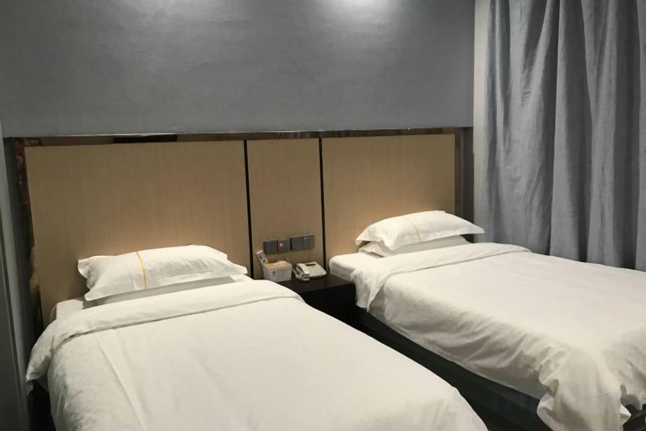 A hotel room with two single beds, a wooden headboard, a bedside table with a phone, and a curtain.