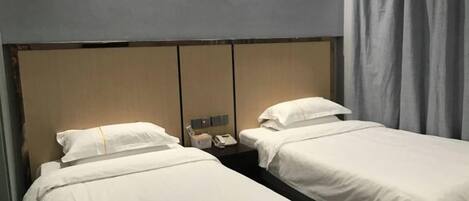 Ein Hotelzimmer mit zwei Einzelbetten, einem Holzkopfteil, einem Nachttisch mit Telefon und einem Vorhang.