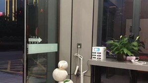 Un hall d’hôtel moderne avec un comptoir d’accueil, un écran numérique et une plante décorative.