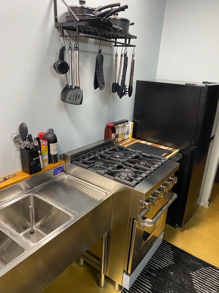 A kitchen with stainless steel appliances, including a stove and oven, a sink, and a black refrigerator.