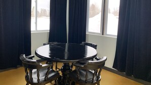 A room with a round table and six chairs, large windows with dark curtains, and a view of a snowy landscape.