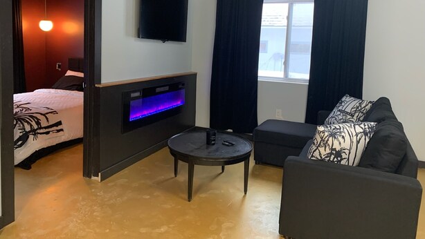 A modern room with a bed, a sofa, a small table, a TV, and a fireplace with a blue light.