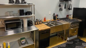 A compact kitchen with a microwave, toaster, sink, and stove. There are shelves with dishes and a 'BAR' sign.