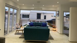 Ett modernt vardagsrum med en grön soffa, ett litet bord och utsikt över en byggnad som är märkt med "T2".