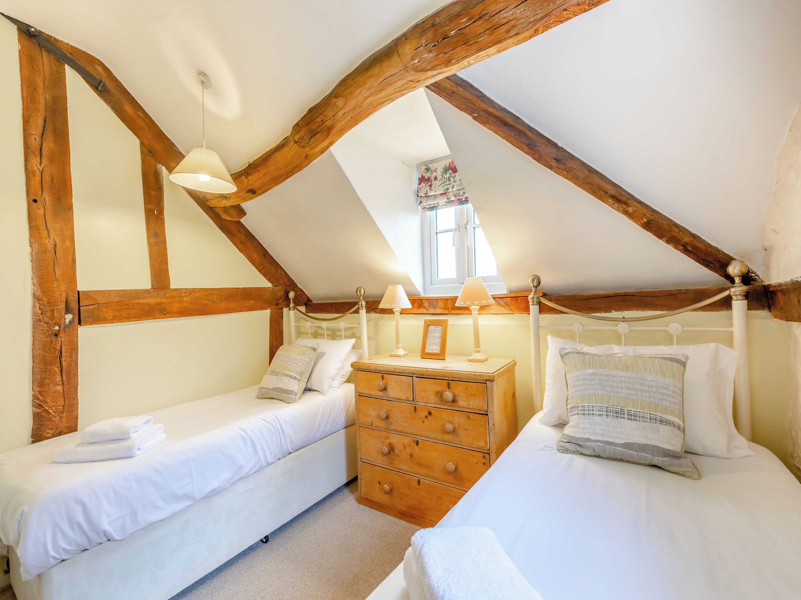 Une chambre avec deux lits simples, des têtes de lit en bois, une commode en bois et une fenêtre donnant sur l’extérieur.