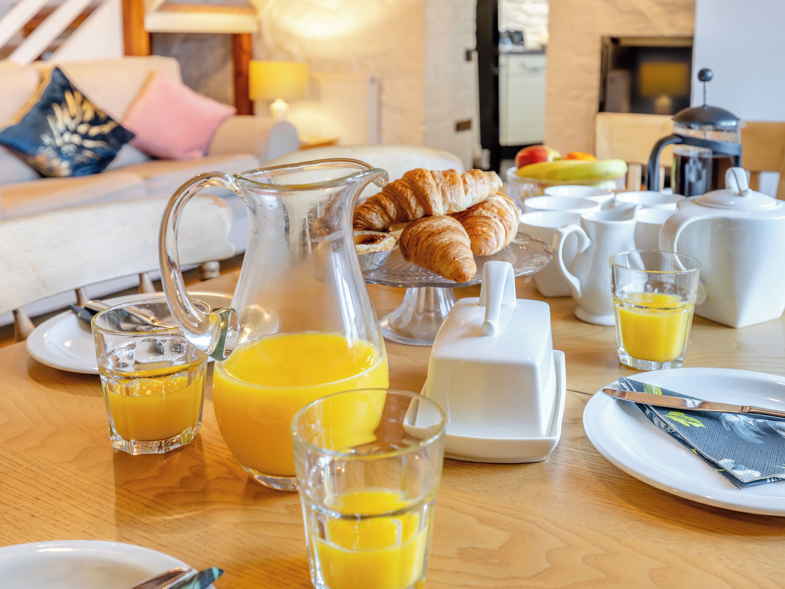 Une table mise pour le petit-déjeuner avec des croissants, du jus et le matériel nécessaire pour préparer du café.