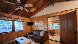 A wooden interior with a sofa, a table, a ceiling fan, and a TV mounted on the wall.