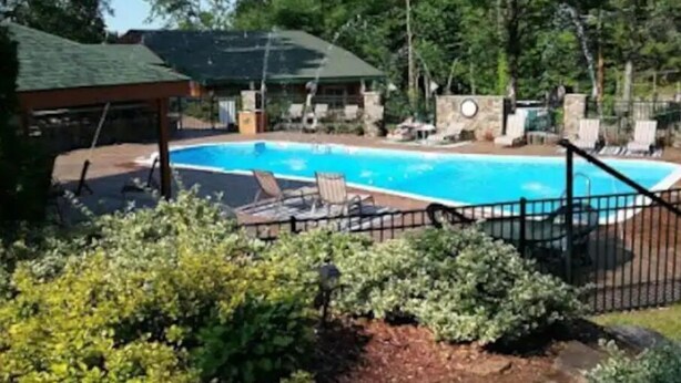 A swimming pool with lounge chairs and a covered area, surrounded by trees and a stone wall.