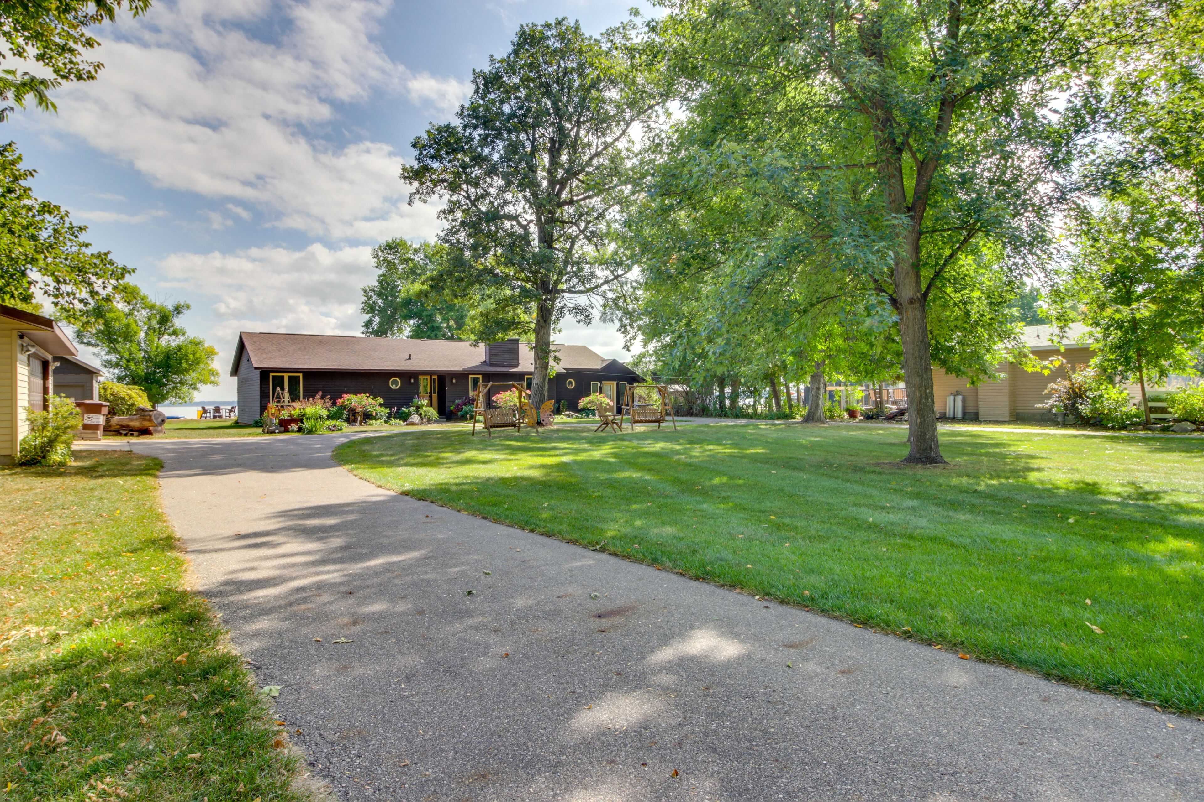 A residential property with a paved driveway leading to a house with a dark roof and a porch.