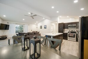 A modern kitchen with a dining area, a flat-screen TV mounted on the wall, and a ceiling fan.