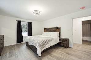 A bedroom with a wooden bed, a nightstand, a dresser, and a window with curtains.