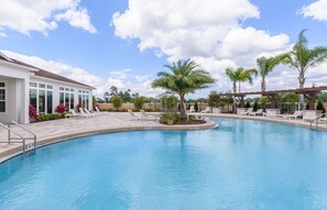 Ein Swimmingpool mit Liegestühlen und Palmen, umgeben von einem Gebäude mit großen Fenstern.