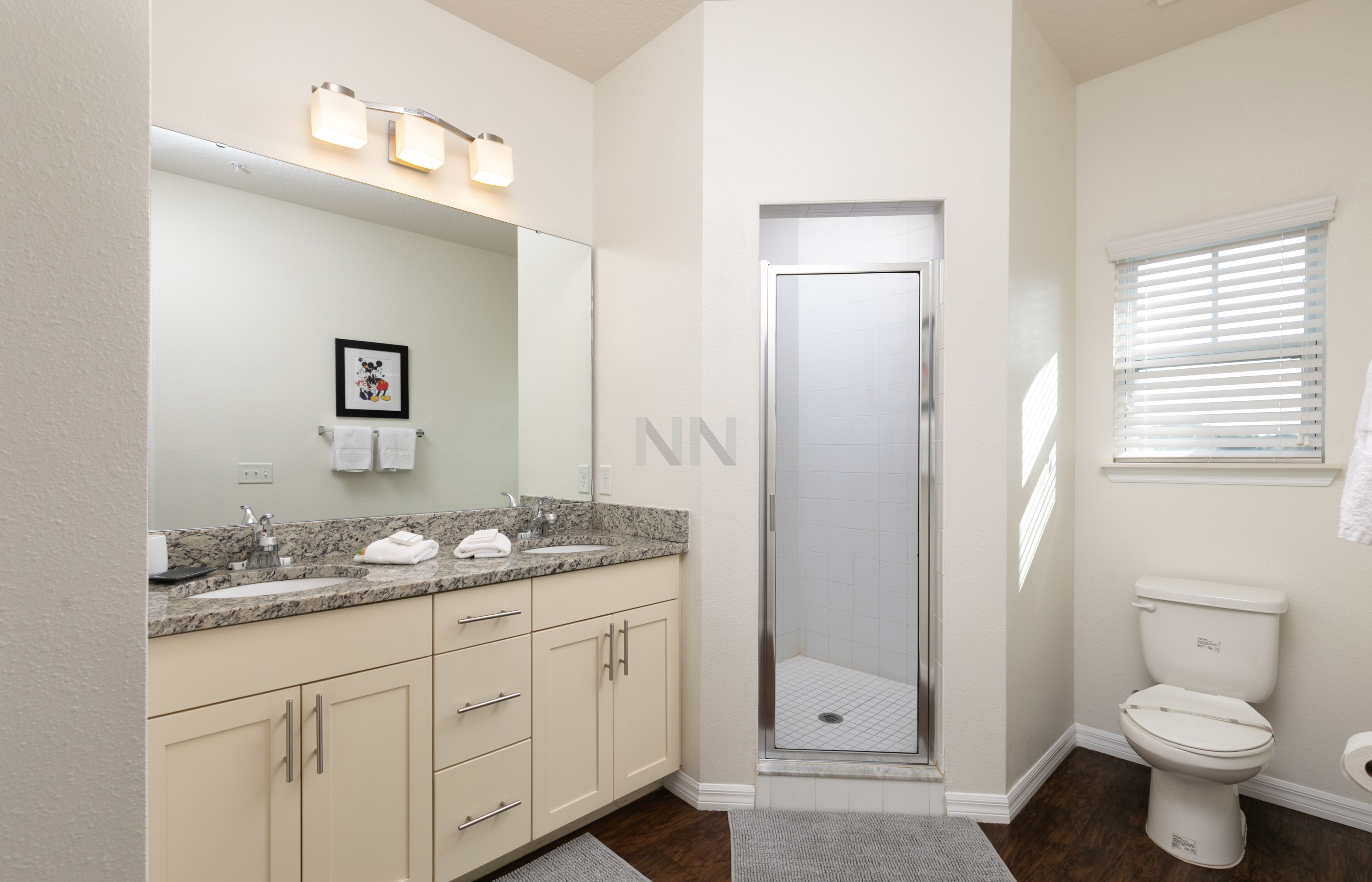 A modern bathroom with a granite countertop, a glass shower enclosure, a toilet, and a framed picture on the wall.
