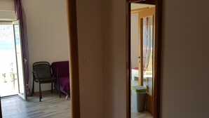 Un pasillo con piso de madera, un espejo en la pared y una puerta que da a otra habitación.