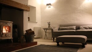 Un salon chaleureux avec un poêle à bois, un canapé et une petite table sur laquelle est posé un vase.
