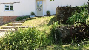 Un bâtiment rustique avec une porte blanche, une petite fenêtre et une enseigne sur laquelle on peut lire : « La Grange aux Fleurs ».