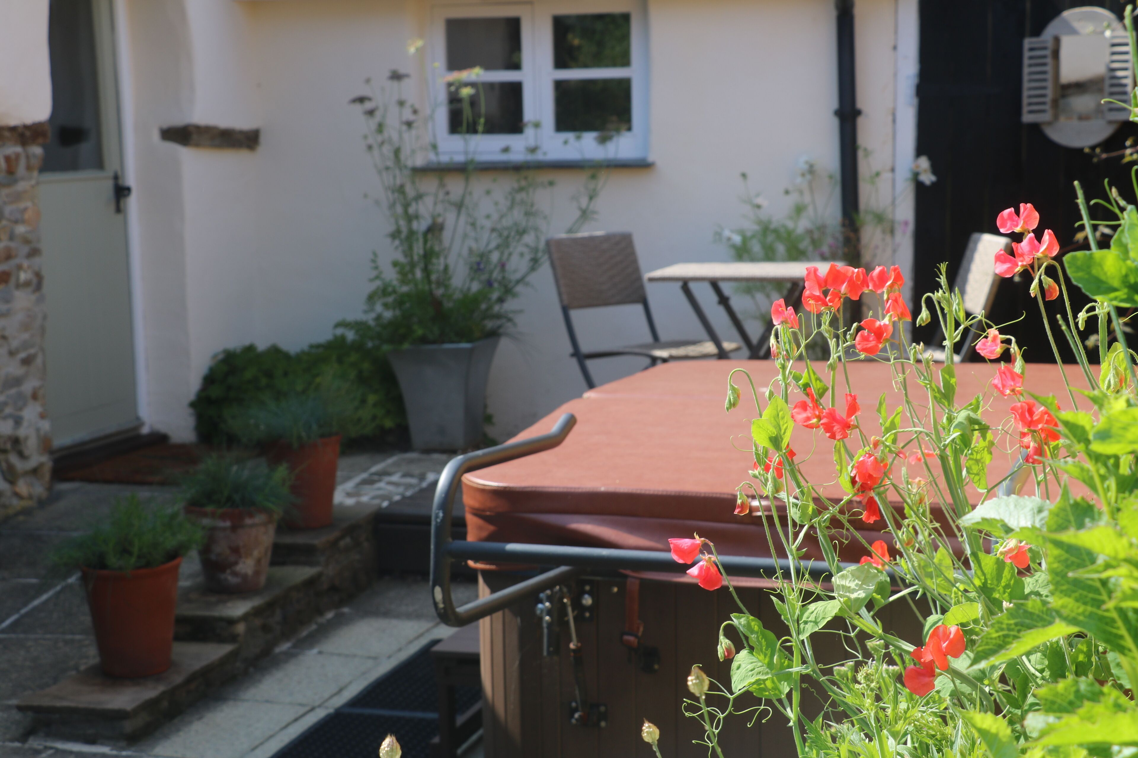 Un patio con mesa y sillas, rodeado de plantas en macetas y un pequeño jardín.