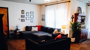 A cozy living room with a sectional sofa, a small side table with a lamp, and a cabinet with decorative items.